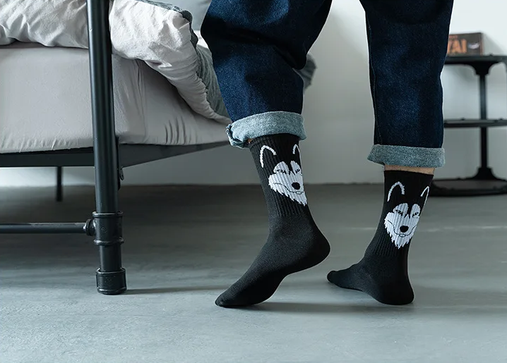 Person wearing black socks with husky designs in a bedroom setting