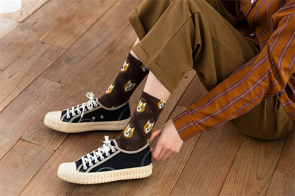 Person wearing black sneakers with white laces and brown socks with a pattern, sitting on a wooden floor.