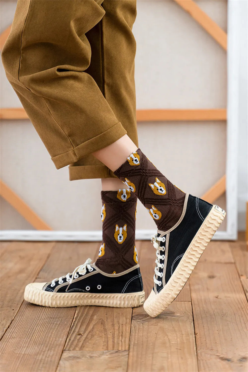 Person wearing brown socks with dog pattern and black sneakers on a wooden floor.