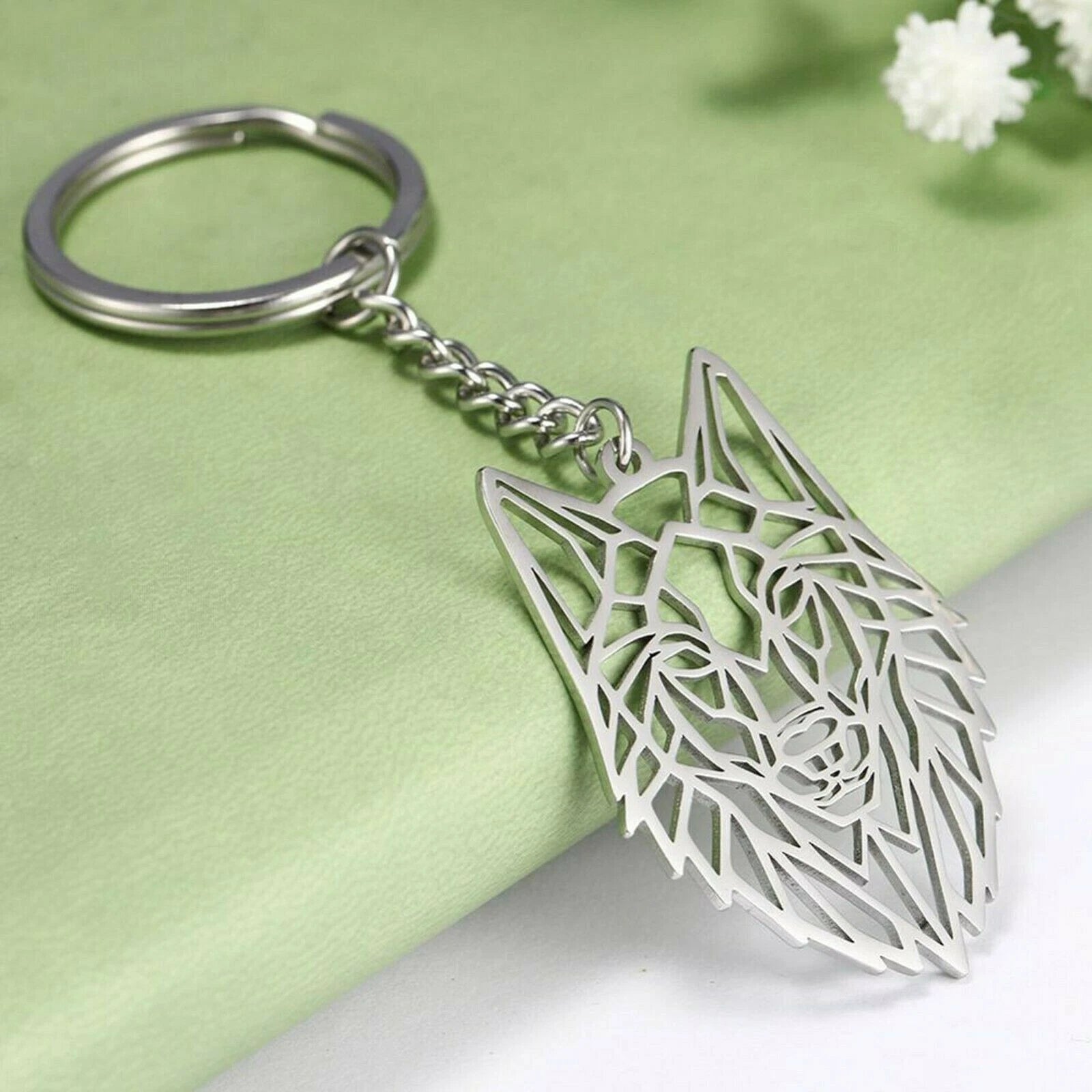 Silver geometric wolf head keychain on a light green fabric background